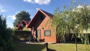 Une cabane rustique avec un toit en pente, une petite véranda et une statue d’oiseau au premier plan.