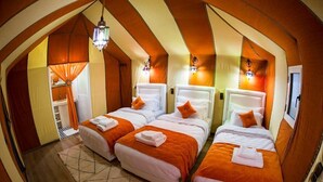 Una habitación con tres camas, cada una con cabecero blanco y ropa de cama naranja. Hay luces fijadas en la pared y una lámpara colgante.