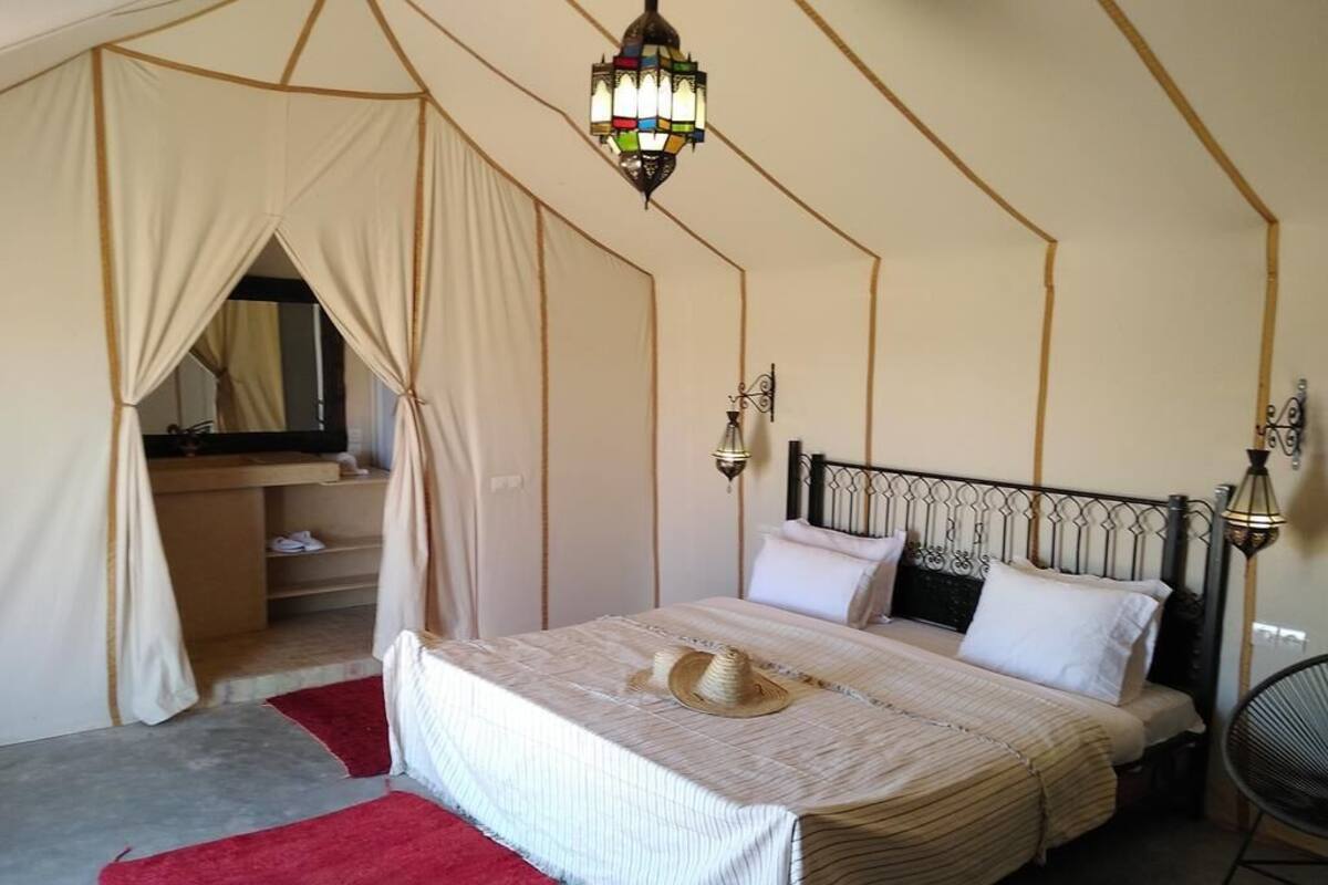 Une chambre aménagée comme une tente, avec un lit, un luminaire suspendu et une chaise.