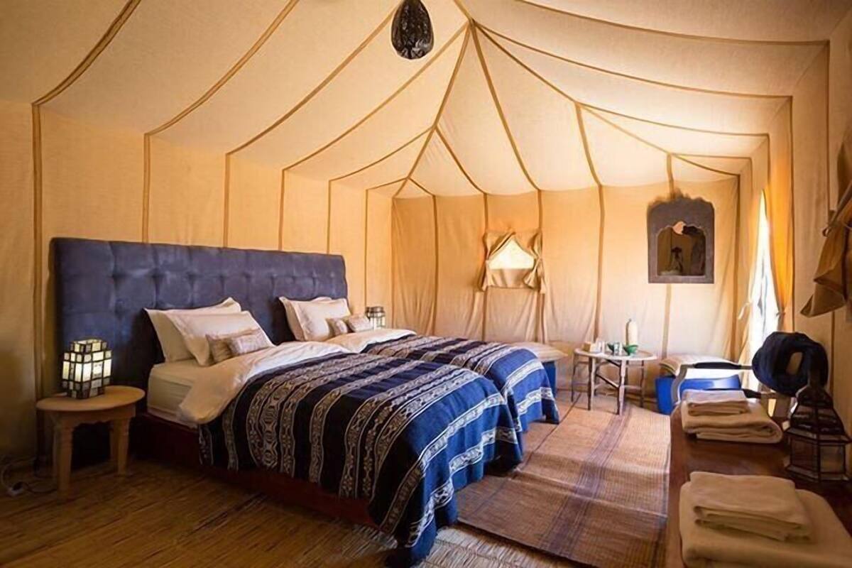 Une chambre aménagée comme une tente, avec deux lits, une table de chevet, une lampe et une petite table.