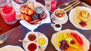 Desayuno con diversos platos, como huevos, frutas, bollería y bebidas.