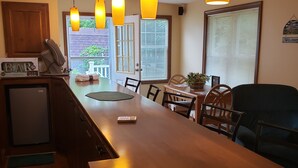 Una cocina con una isla central, luces colgantes, un refrigerador y un comedor con sillas y una mesa.