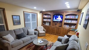 Una sala de estar con un sofá gris, un sillón a rayas, una mesa de centro y un televisor montado en un mueble de madera.