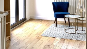 A room with a blue chair, a round glass table, a hanging light fixture, and a bookshelf.