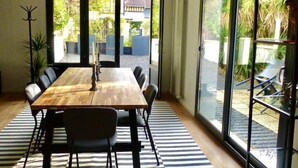 A dining area with a wooden table and chairs, a striped rug, and large glass doors leading to a garden.