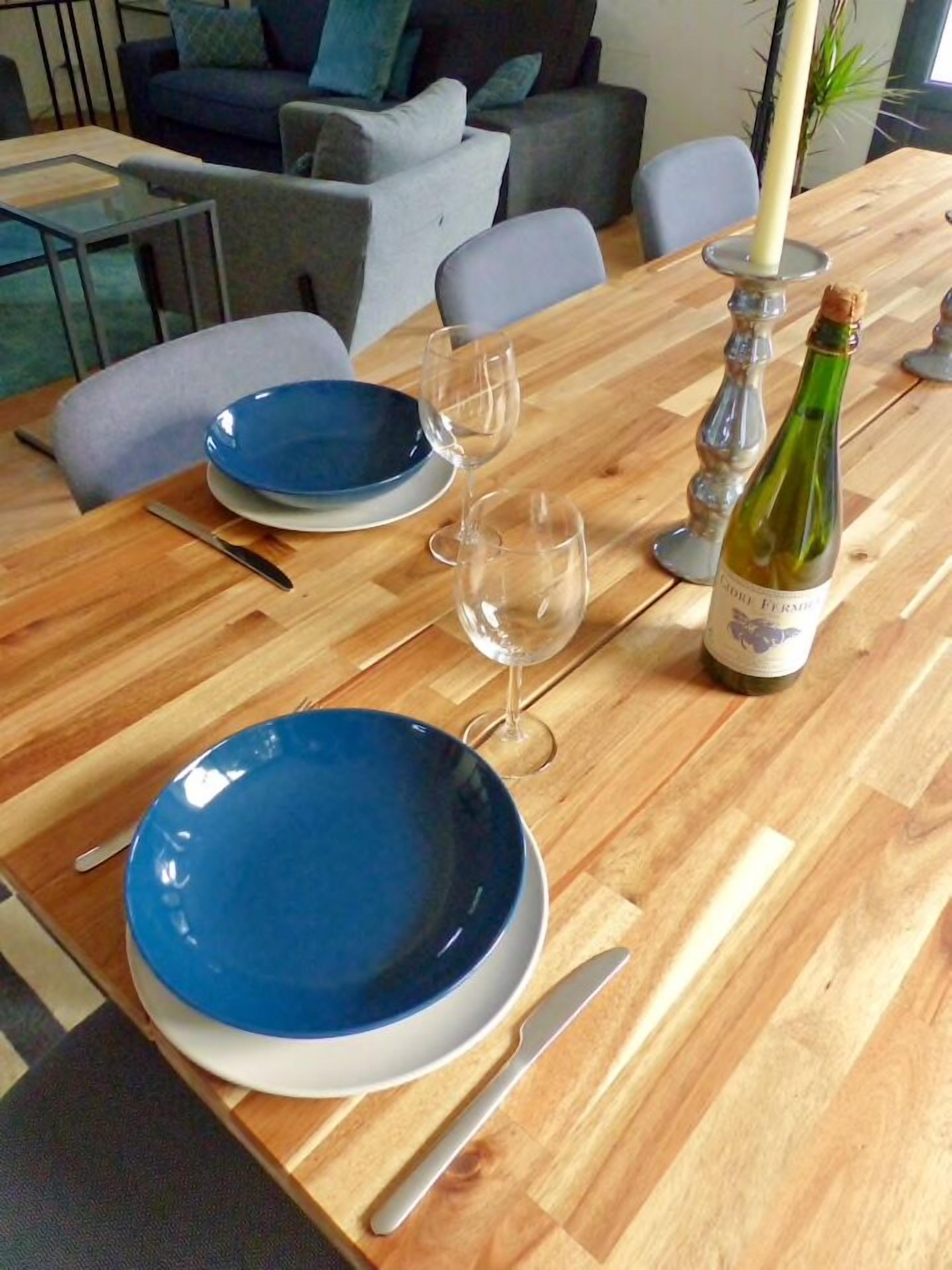 A dining table set with blue plates, wine glasses, a bottle of wine, and a candle.