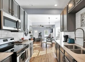 A modern kitchen with stainless steel appliances, a wooden floor, and a dining area with a chandelier. - New! Cozy, Charming Getaway in Heart of Atl (Atlanta)