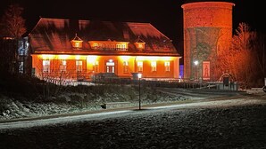 Un grand bâtiment doté d’une tour imposante, d’une galerie couverte et d’une zone pavée devant l’entrée.