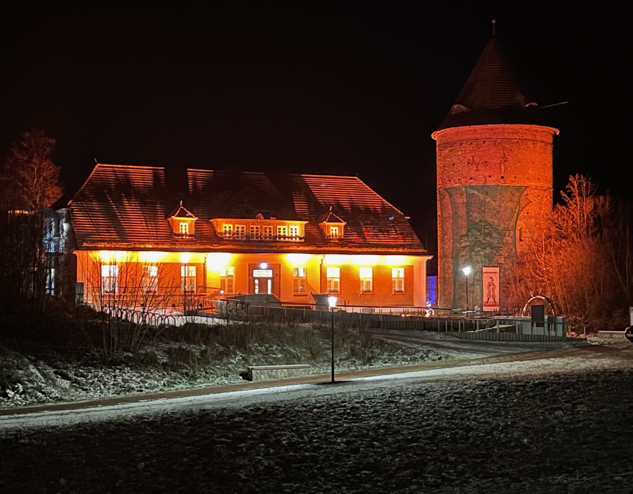 A large building with a prominent tower, a covered walkway, and a paved area in front.