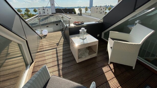 Une terrasse sur le toit, dotée d'un sol en bois, de meubles en osier blanc et offrant une vue sur le paysage urbain.