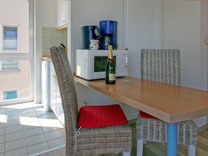 Un coin repas avec des chaises en osier, une table en bois et une bouteille de vin.