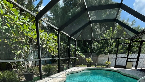 Una piscina de diseño curvo, rodeada por un área techada con cerramiento de metal.