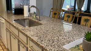 Una cocina con encimeras de granito, pileta de acero inoxidable y muebles de color blanco.