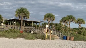 Una playa con una estructura de madera, palmeras y una escalera que lleva a un área techada.