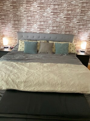 Una cama con cabecera gris, varios almohadones y una colcha estampada.