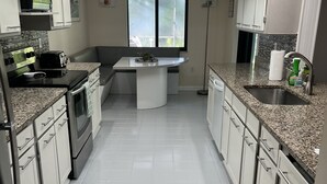 Una cocina moderna con armarios blancos, encimera de granito, horno empotrado y ventilador de techo.