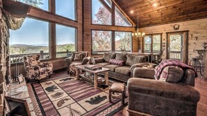 A cozy cabin interior with a large window, wooden furniture, and a stone fireplace.