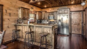 A rustic kitchen with wooden cabinets, a stainless steel refrigerator, and a bar area with stools.