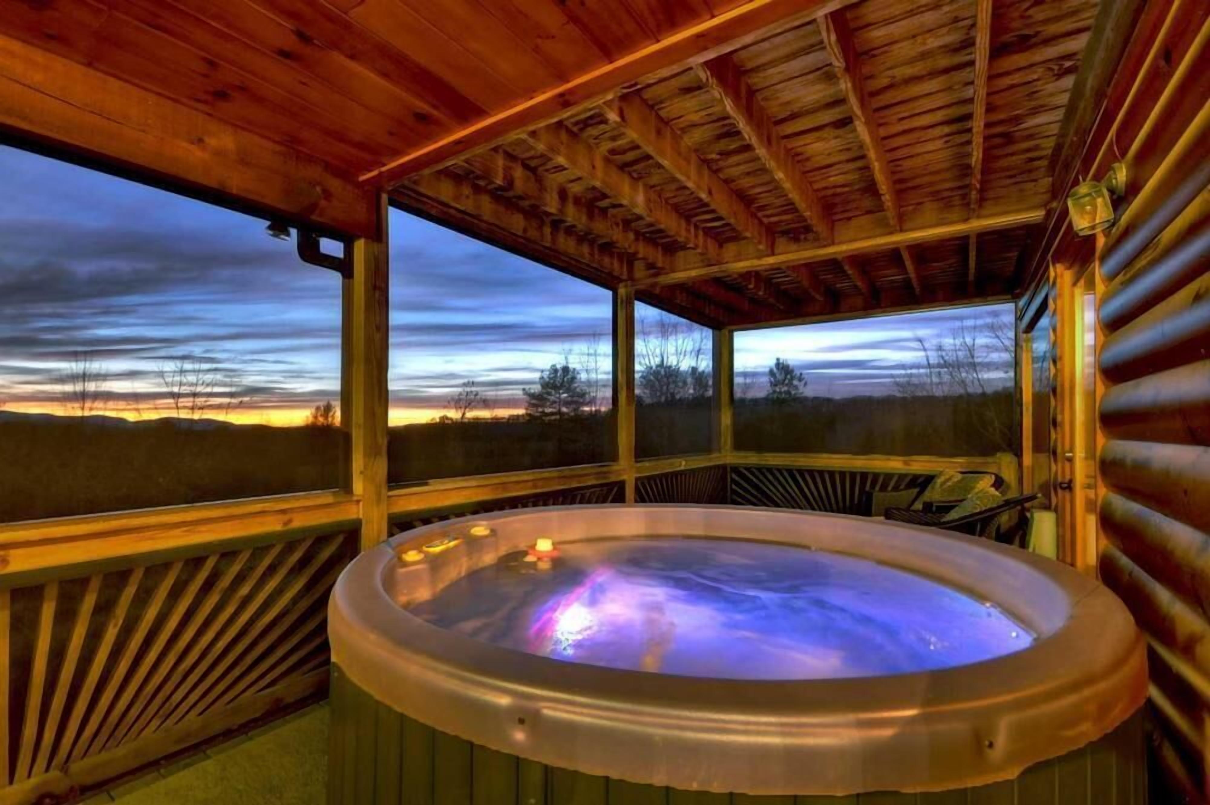 A hot tub in a wooden cabin with a view of a sunset over a field.