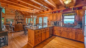 A spacious kitchen with wooden cabinets, a large island, and a stone fireplace. - Rocky Top- Pet Friendly | VIEWS VIEWS VIEWS! | Large Screened Porch (Morganton)
