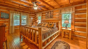 A log cabin bedroom with a wooden bed, a ceiling fan, and a window with curtains. - Rocky Top- Pet Friendly | VIEWS VIEWS VIEWS! | Large Screened Porch (Morganton)