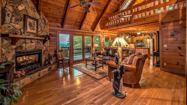 A cozy cabin interior with a stone fireplace, leather sofa, and a dining area. - Rocky Top- Pet Friendly | VIEWS VIEWS VIEWS! | Large Screened Porch (Morganton)