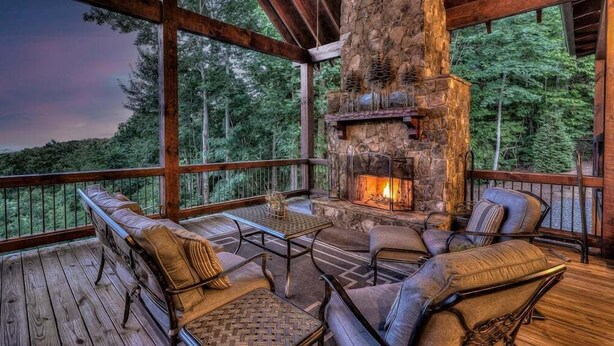 Une terrasse en bois avec une cheminée en pierre, un espace salon et une vue sur la forêt.