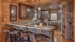 A rustic kitchen with wooden cabinets, a marble island, bar stools, and a hanging light fixture.