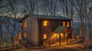 A log cabin with a porch and deck, surrounded by trees.