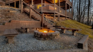 A wooden deck with a fire pit, steps leading up to a cabin, and a bench.
