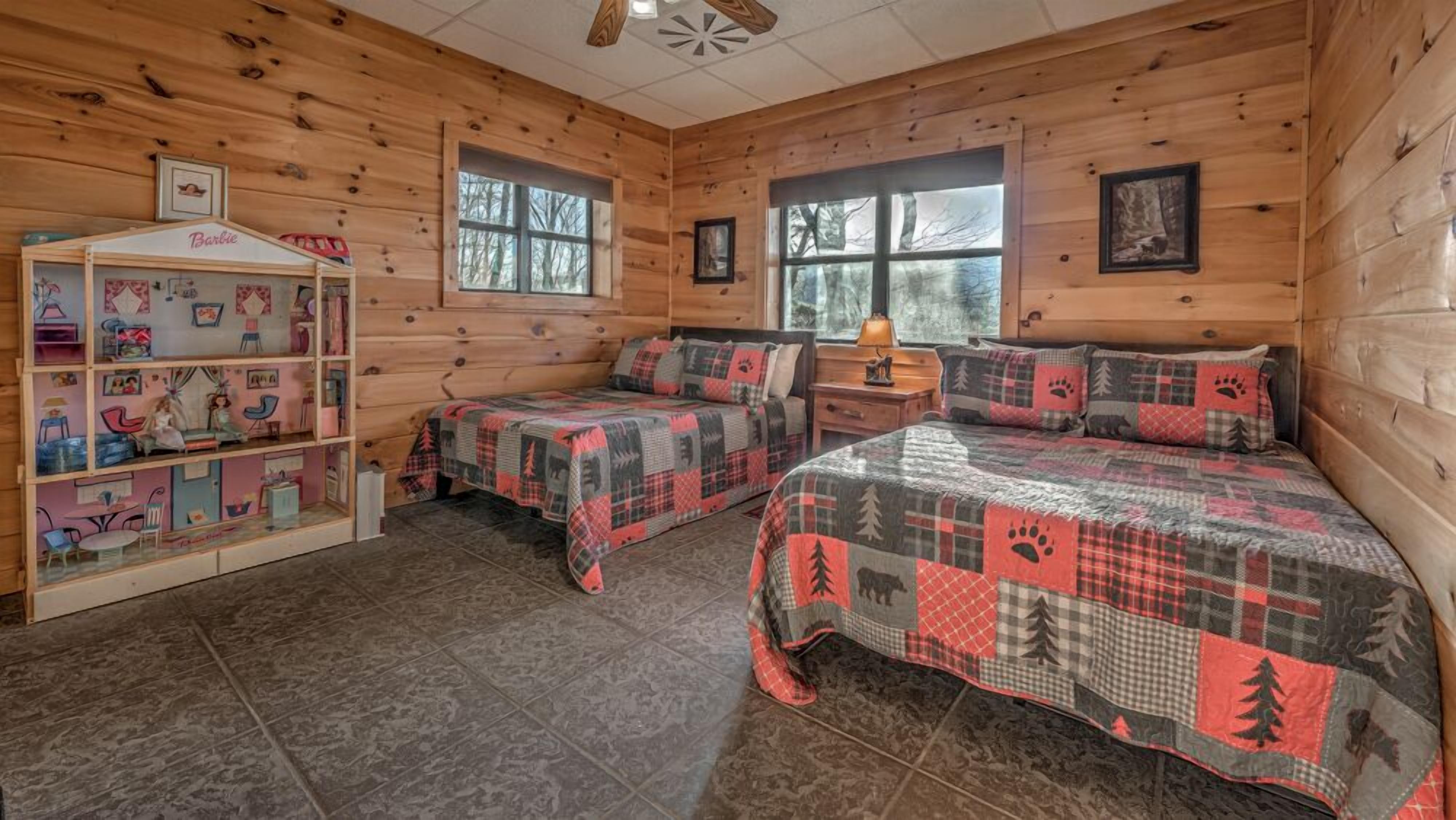 Quarto no estilo de cabana com duas camas, um espaço para brincar com tema Barbie e amplas janelas.