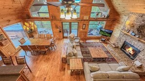 Een gezellig cabin interieur met een eethoek, zitplaatsen, een open haard en grote ramen.