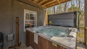 Un bain à remous situé dans un espace extérieur abrité, doté d’une terrasse en bois, d’une fenêtre et offrant une vue sur les arbres.