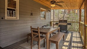 Une cabane en bois avec un porche couvert, une table à manger avec des chaises, un banc et un barbecue.