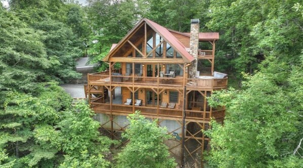 Une cabane en bois à plusieurs niveaux, dotée de balcons et entourée d’une forêt dense.