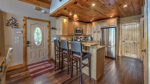 A spacious kitchen with wooden cabinets, a stainless steel refrigerator, and a bar area with stools.
