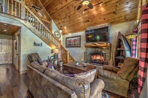 A cozy living room with a fireplace, wooden ceiling, and a staircase.