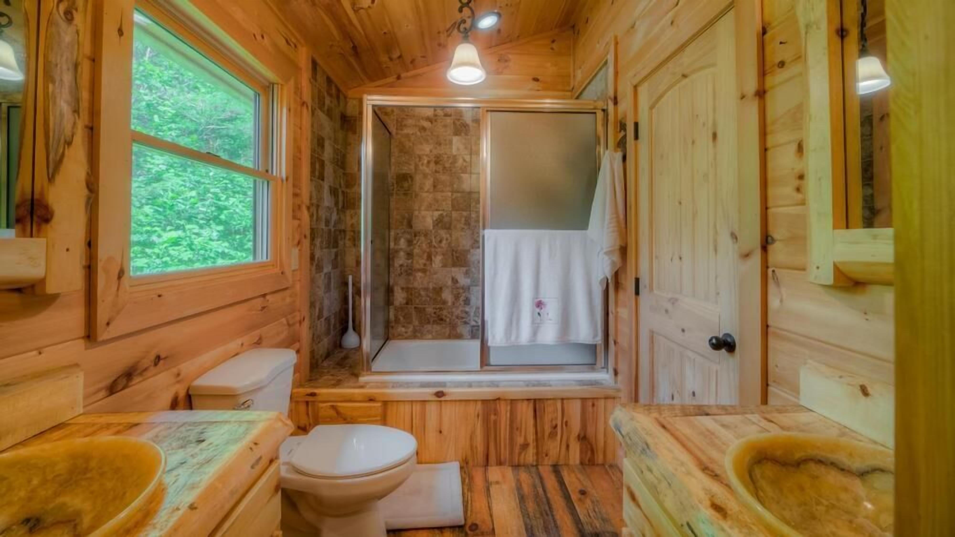 A wooden cabin bathroom with a toilet, sink, and shower.