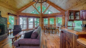 A cabin interior with a fireplace, seating area, dining space, and a kitchen. - Southern Comfort- Lake Front | 2 Level Dock | Paved Roads and Driveway (Morganton)