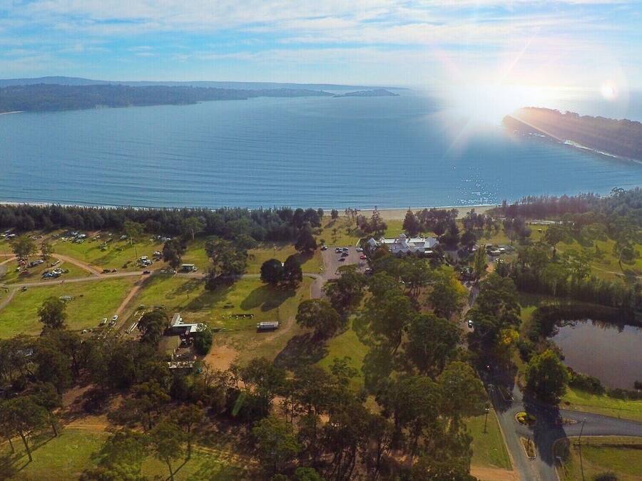 Vista aérea de una zona costera con una gran masa de agua, un pequeño poblado con edificios y coches aparcados, y una carretera que conduce al agua.
