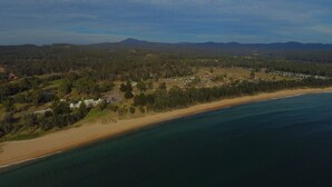 Vista aérea de una zona costera con playa, edificios residenciales y una cadena montañosa al fondo.