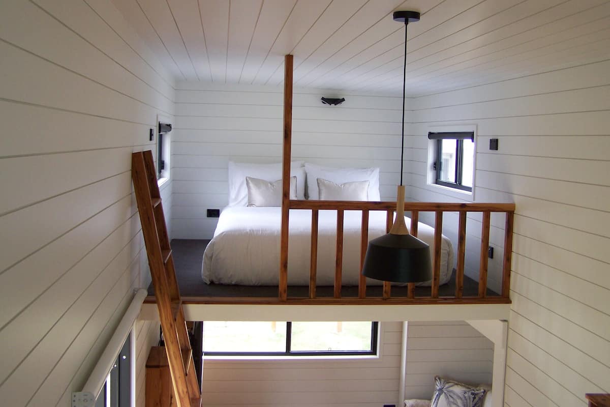 Ein Schlafzimmer mit Hochbett, Holzbalkon, Pendelleuchte und einem Fenster für natürliches Licht.
