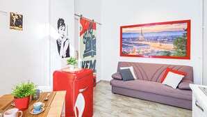A modern living room with a sofa, a red appliance, a dining table with cups and a plant, and a cityscape painting. - Very central - Via Po Torino (Torino)