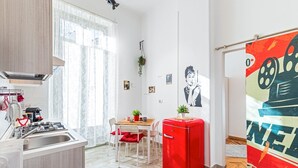 A modern kitchen with a red refrigerator, a dining area with a wooden table and chairs, and a large window providing natural light. - Very central - Via Po Torino (Torino)