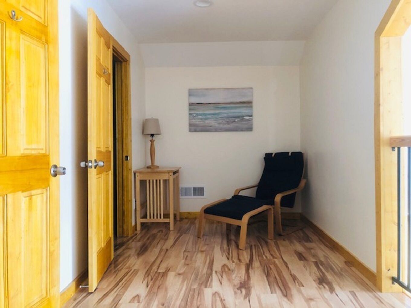 Un couloir avec un plancher en bois, une porte en bois, une petite table avec une lampe et une chaise.