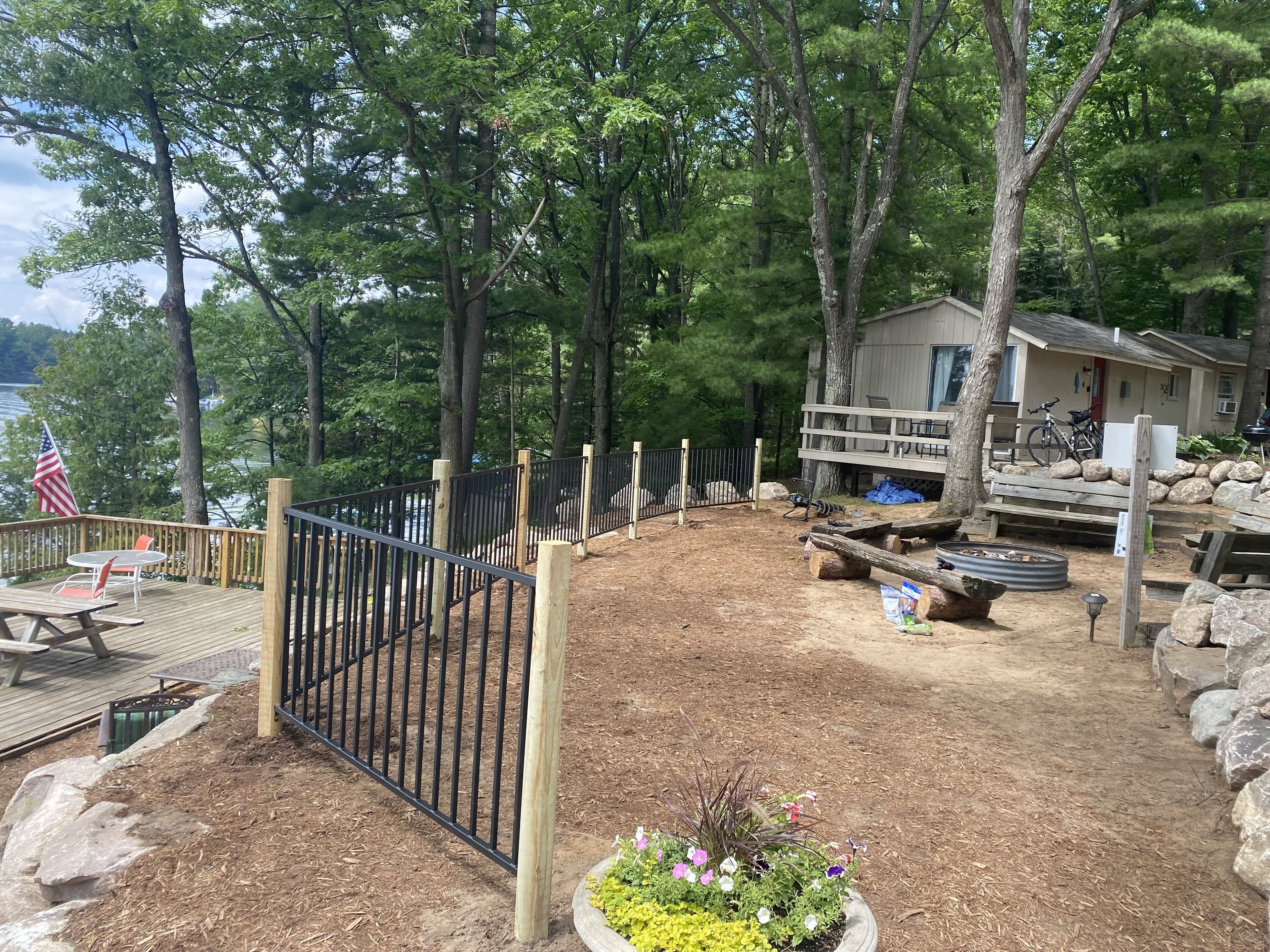 A deck with picnic tables and a flag, surrounded by a fenced area with a wooden deck and a house with a balcony.