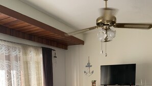 A living room with a bed, a television on a wooden stand, a ceiling fan, and a window with curtains. - Lindo apartamento a una cuadra de la Playa Brava. (Punta del Este)