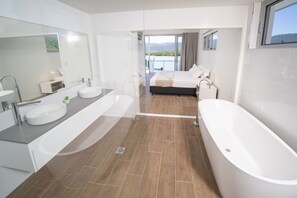 A modern bathroom with a large bathtub, a double sink, and a large mirror. - Harbour Cove (Airlie Beach)