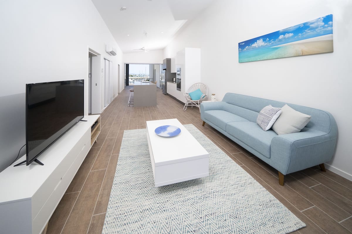 A modern living room with a flat-screen TV, a light blue sofa, a white coffee table, and a large painting of a beach scene.