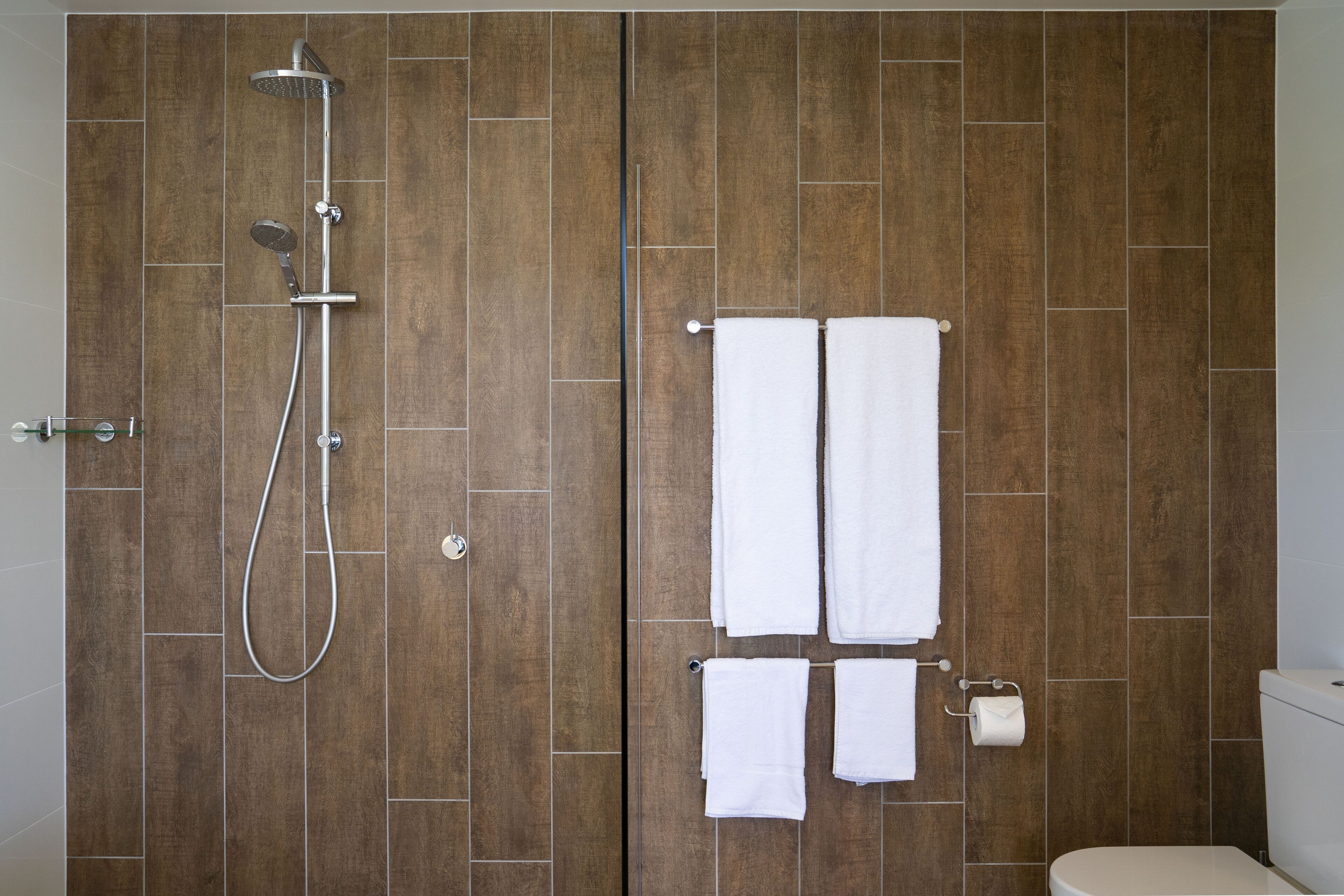 A bathroom with wooden walls, a shower, and two white towels hanging on hooks.